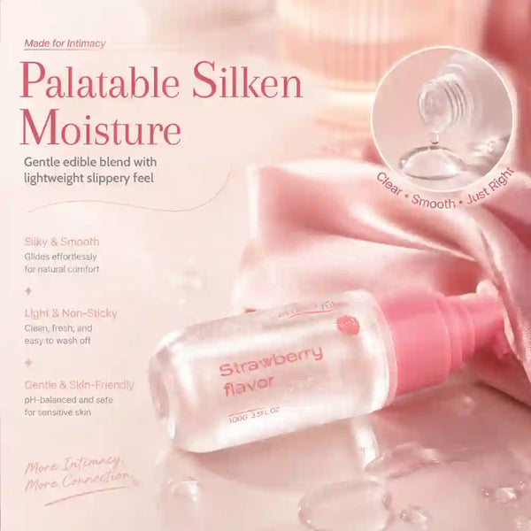 A bottle of Palatable Silken Moisture Strawberry flavor edible oil serum shown on a soft pink background with satin fabric and droplets. The bottle is clear with a pink cap, and the image includes descriptive text and a droplet close-up inset.