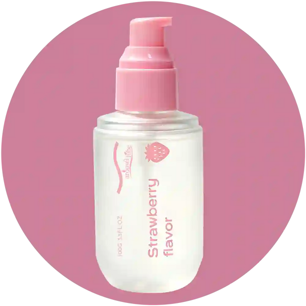 A clear plastic pump bottle of facial cleanser with a pink pump dispenser, labeled 'Strawberry flavor' by the brand 'natural life', centered on a pink circular background.
