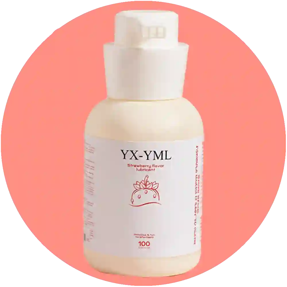 A bottle of YX-YML strawberry flavor lubricant stands next to its white box on a pink surface, with strawberries and a pink floral vase in the background.