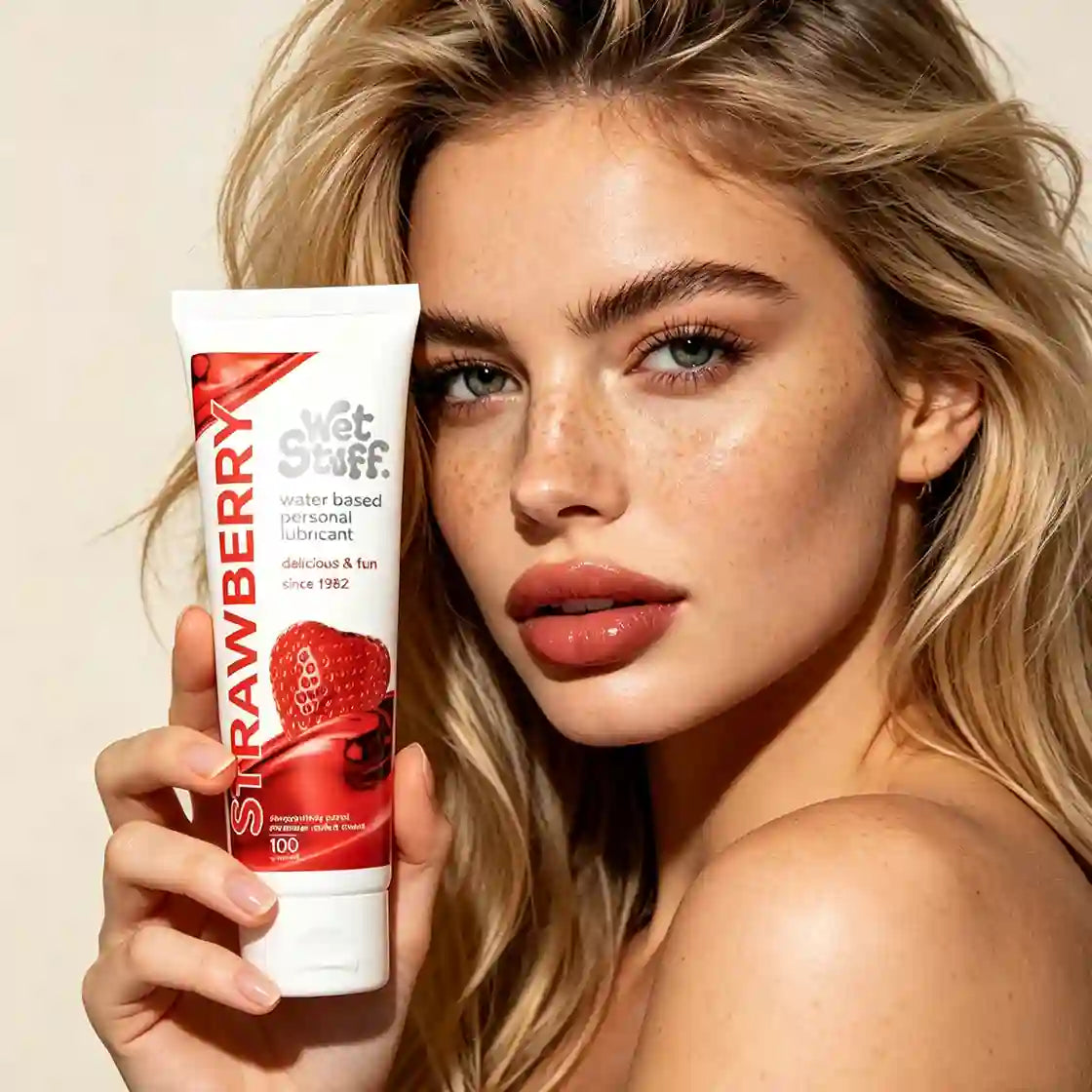 Woman holding a strawberry-flavored lubricant tube against a beige for dry private part use
