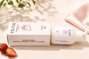 YX-YML Strawberry personal lubricant bottle and its white packaging box, styled on a warm beige surface with a pink satin cloth, fresh strawberries, and soft leaf shadows.