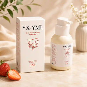 A bottle of YX-YML strawberry flavor lubricant and its white box are displayed on a beige surface with decorative props including a strawberry, leaves, and a vase in the background.