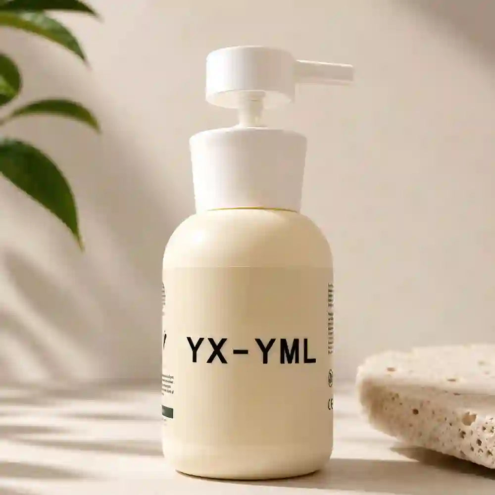 A cream-colored pump lube bottle with black text reading 'YX-YML' on the front, set on a light surface with soft shadows. A green leaf and a textured stone slab are visible in the background.