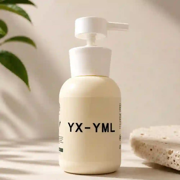 A cream-colored pump lube bottle with black text reading 'YX-YML' on the front, set on a light surface with soft shadows. A green leaf and a textured stone slab are visible in the background.