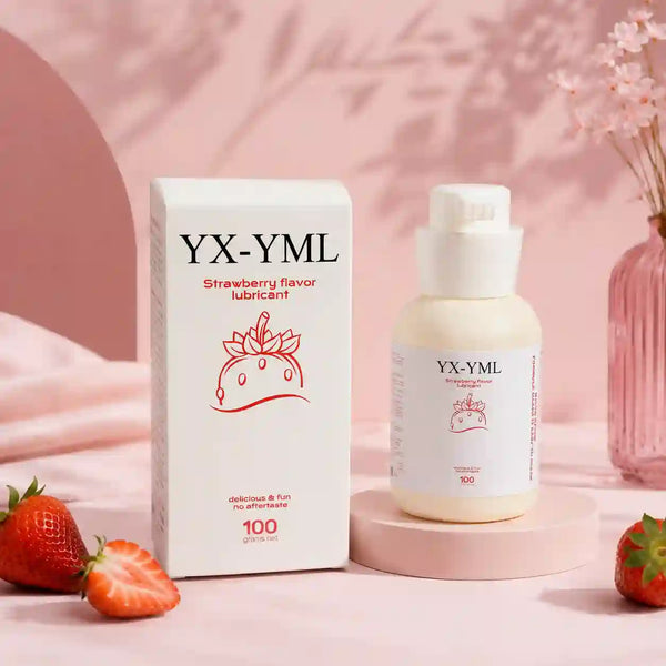 A bottle of YX-YML strawberry flavor lubricant stands next to its white box on a pink surface, with strawberries and a pink floral vase in the background.