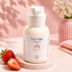 A bottle of YX-YML Strawberry Lubricant centered on a pink surface with strawberries in the foreground and a pink vase of flowers in the background.